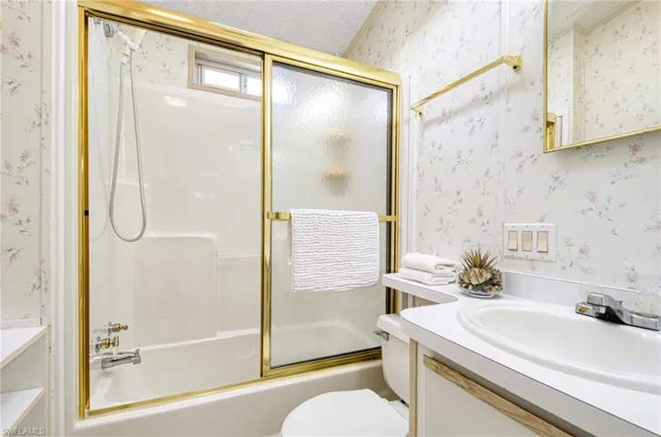 Full bathroom with vanity, toilet, enclosed tub / shower combo, and a textured ceiling