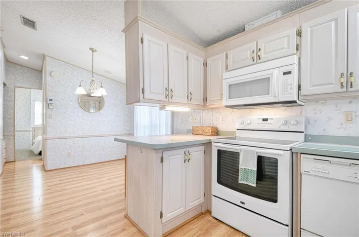 Kitchen featuring white appliances, light hardwood / wood-style flooring, a notable chandelier, white cabinets, and hanging light fixtures