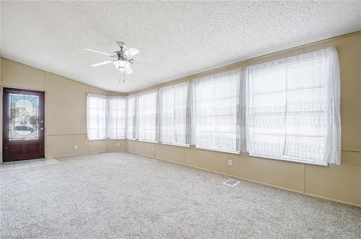 Spare room featuring a textured ceiling, ceiling fan, light colored carpet, and lofted ceiling