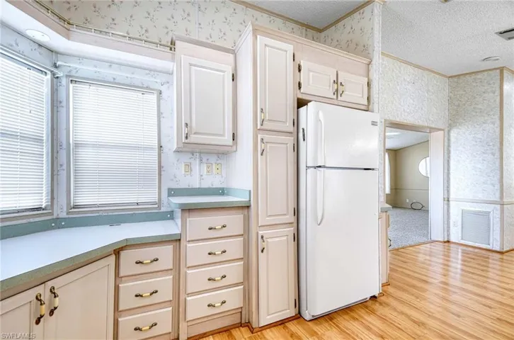 Kitchen with white refrigerator, crown molding, light hardwood / wood-style floors, and a textured ceiling