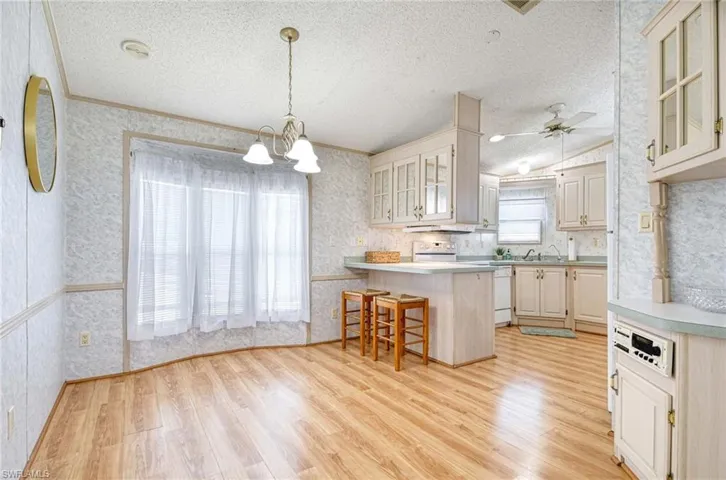 Kitchen featuring hanging light fixtures, a kitchen breakfast bar, light hardwood / wood-style flooring, white dishwasher, and ceiling fan with notable chandelier