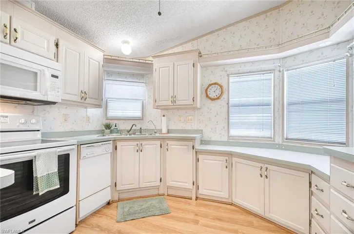 Kitchen with white cabinetry, sink, light hardwood / wood-style floors, a textured ceiling, and white appliances