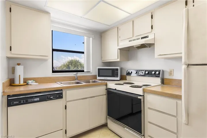 Kitchen featuring range hood, white appliances, sink, and light tile floors