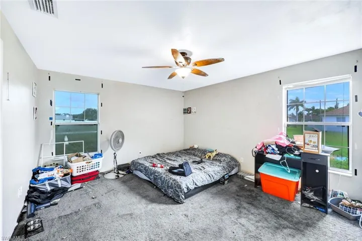Carpeted bedroom with ceiling fan and multiple windows
