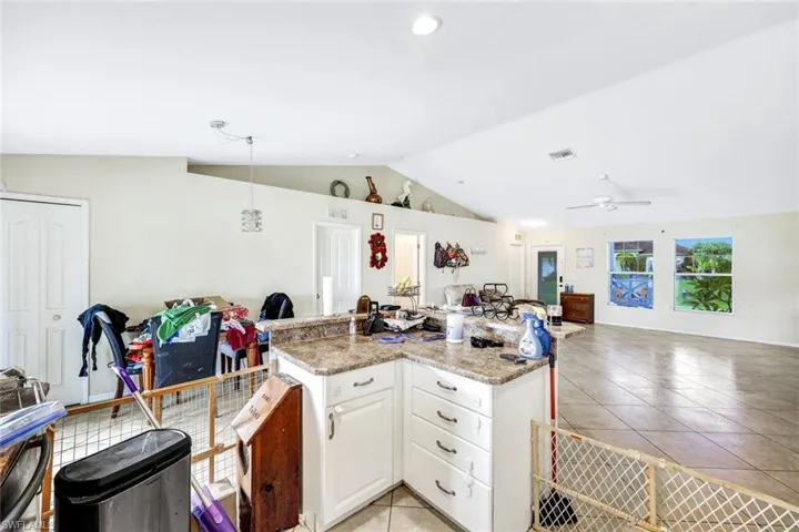 Kitchen featuring ceiling fan, light tile flooring, light stone counters, lofted ceiling, and white cabinetry