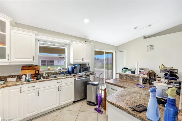 Kitchen with dishwasher, decorative light fixtures, light tile floors, white cabinets, and lofted ceiling