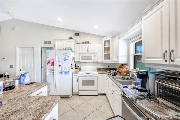 Kitchen with vaulted ceiling, white cabinetry, sink, white appliances, and light tile floors