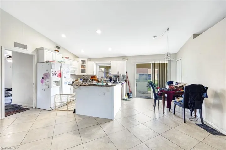 Kitchen featuring white appliances, white cabinets, lofted ceiling, and light tile floors
