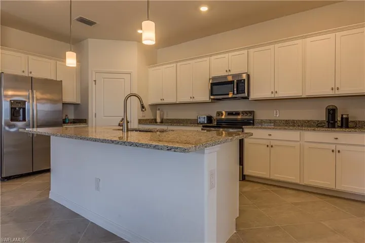 Kitchen with stainless steel appliances, light stone counters, white cabinetry, a center island with sink, and hanging light fixtures