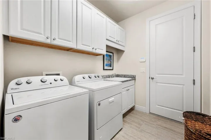 Laundry room featuring cabinets, sink, washing machine and clothes dryer, and light hardwood / wood-style flooring