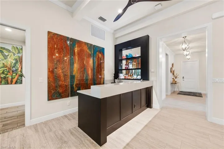 Bar featuring ceiling fan with notable chandelier, decorative light fixtures, beamed ceiling, ornamental molding, and light hardwood / wood-style floors