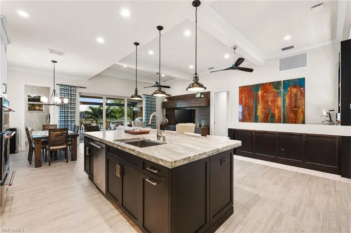 Kitchen featuring pendant lighting, sink, crown molding, light stone counters, and an island with sink