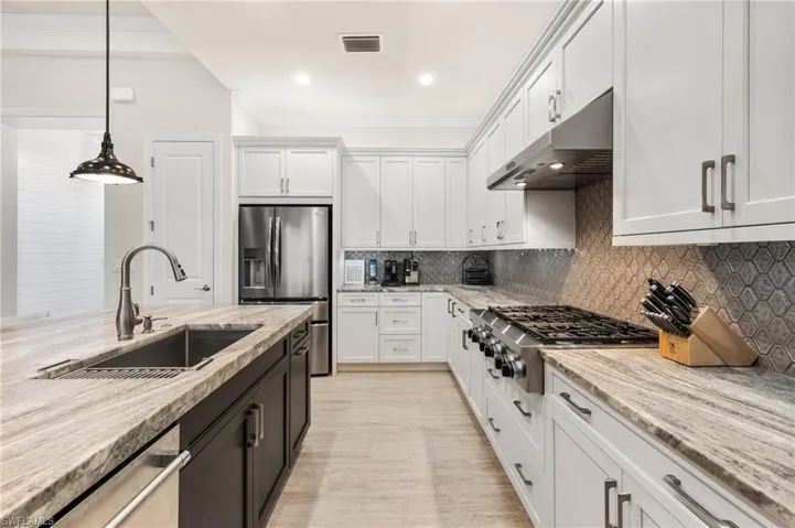 Kitchen with appliances with stainless steel finishes, decorative light fixtures, sink, white cabinets, and light stone countertops