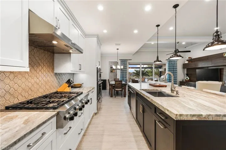 Kitchen with white cabinets, sink, an island with sink, and exhaust hood