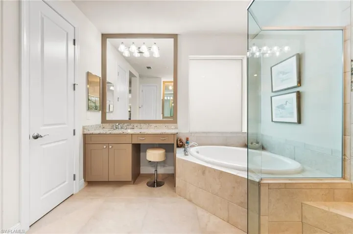 Bathroom featuring a relaxing tiled tub, vanity, and tile patterned flooring