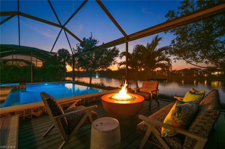 Pool at dusk featuring pool water feature, a water view, glass enclosure, and an outdoor fire pit