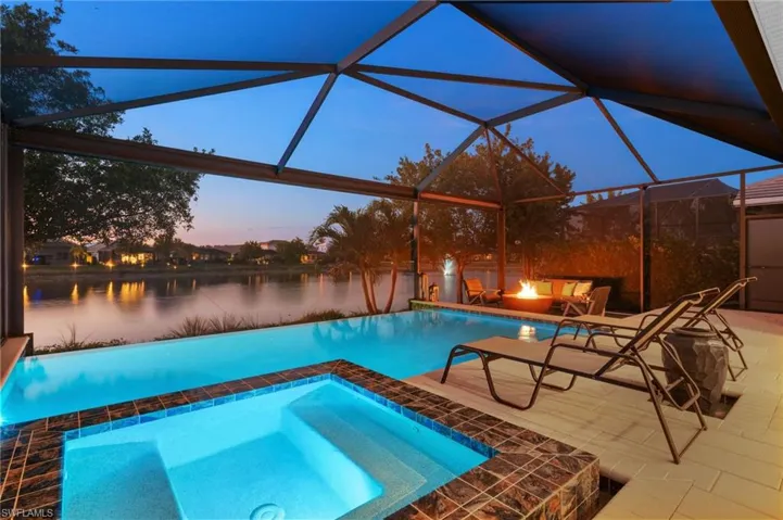 Pool at dusk featuring a lanai, a water view, a patio area, and an outdoor fire pit