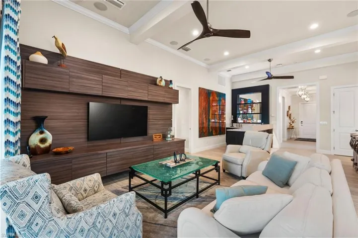 Living room with beamed ceiling, ceiling fan, ornamental molding, and light wood-type flooring