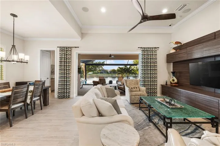 Living room with crown molding, ceiling fan with notable chandelier, and light hardwood / wood-style flooring