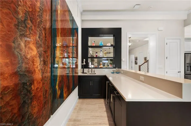 Bar with crown molding, stainless steel fridge with ice dispenser, and light hardwood / wood-style flooring