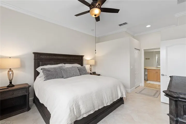 Tiled bedroom with ceiling fan, crown molding, and connected bathroom