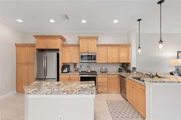 Kitchen with hanging light fixtures, stainless steel appliances, kitchen peninsula, and light brown cabinets