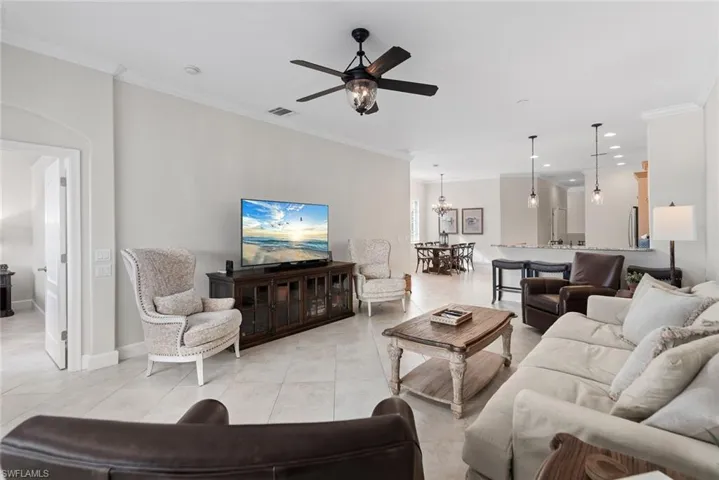 Living room with crown molding, light tile patterned floors, and ceiling fan with notable chandelier