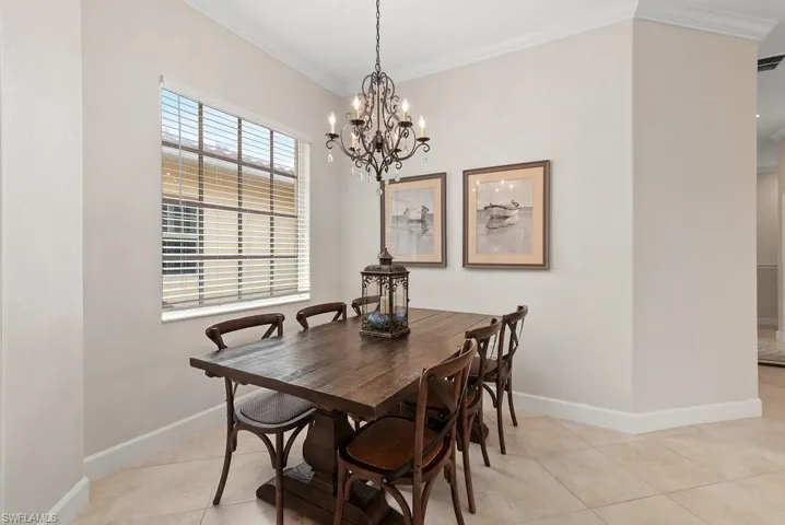 Dining area with ornamental molding, a notable chandelier, and light tile patterned flooring
