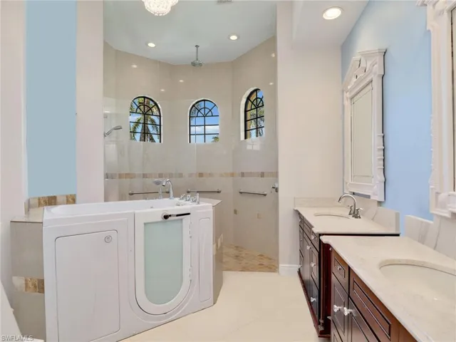 Full bath featuring two vanities, a walk in shower, a sink, and a garden tub