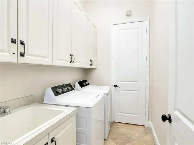 Laundry room featuring baseboards, a sink, light tile patterned flooring, cabinet space, and washer and dryer