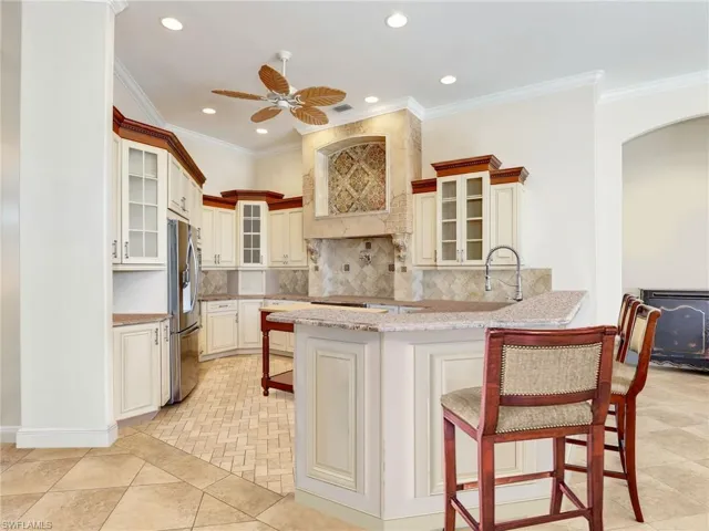 Kitchen with stainless steel refrigerator with ice dispenser, custom range hood, decorative backsplash, arched walkways, and a peninsula