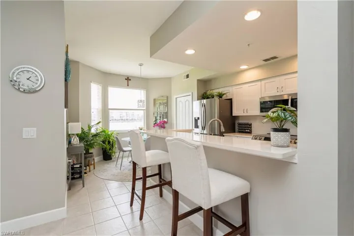 Kitchen featuring pendant lighting, white cabinetry, appliances with stainless steel finishes, light tile patterned floors, and a breakfast bar area