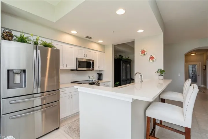 Kitchen featuring stainless steel appliances, tasteful backsplash, white cabinets, light tile patterned floors, and kitchen peninsula