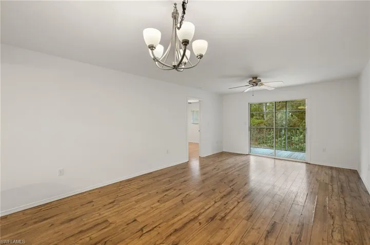 Spare room with ceiling fan with notable chandelier and hardwood / wood-style flooring