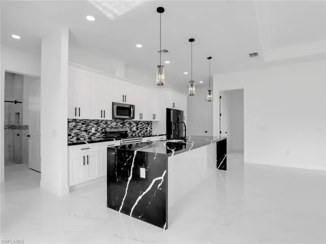 Kitchen featuring decorative light fixtures, appliances with stainless steel finishes, a center island with sink, white cabinetry, and recessed lighting