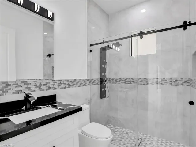 Bathroom featuring vanity, a shower stall, backsplash, and tile walls