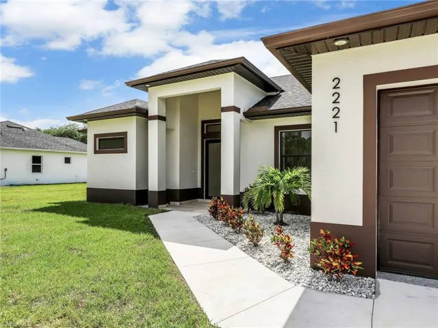 Doorway to property featuring stucco siding, a yard, and roof with shingles