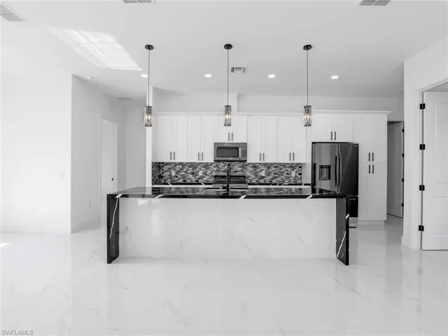 Kitchen featuring white cabinetry, dark stone countertops, a spacious island, decorative light fixtures, and recessed lighting