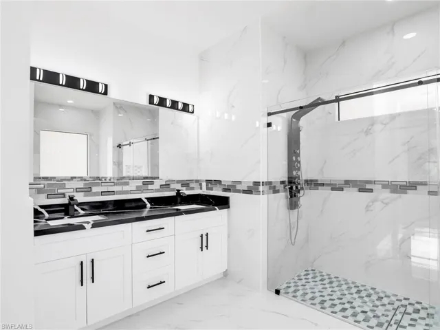 Full bathroom featuring double vanity, a marble finish shower, light marble finish floors, and tile walls