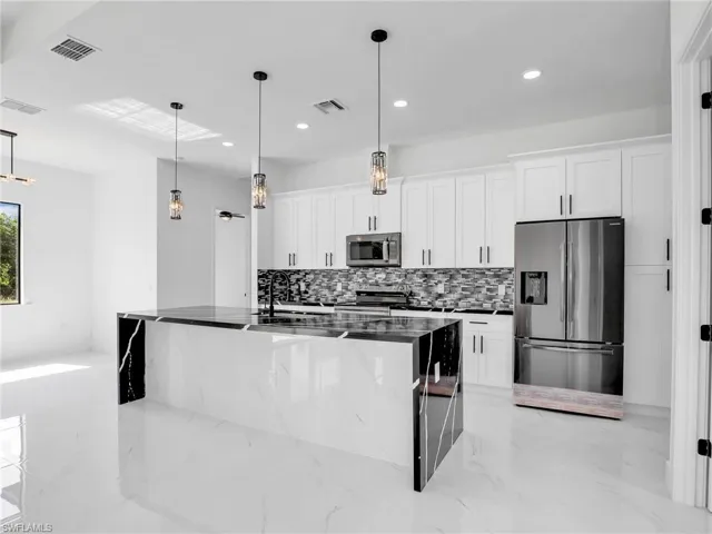 Kitchen featuring appliances with stainless steel finishes, white cabinetry, tasteful backsplash, an island with sink, and recessed lighting