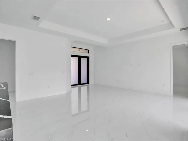 Empty room with a raised ceiling, recessed lighting, and light marble finish floors