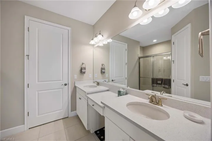 Bathroom with double vanity, light tile patterned floors, and a shower stall