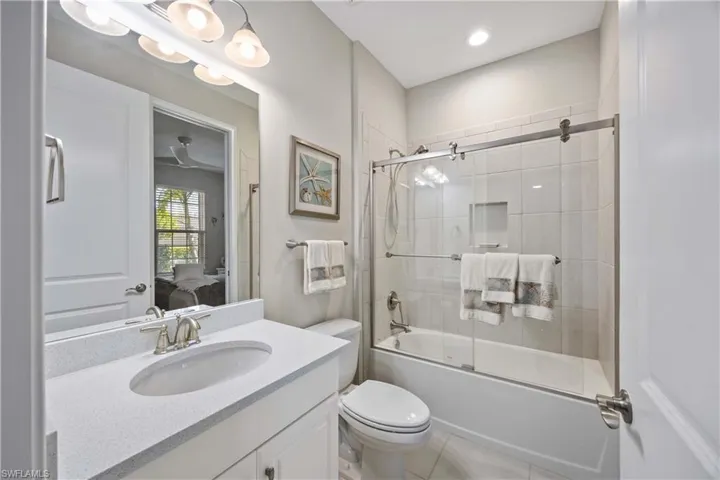 Ensuite bathroom with bath / shower combo with glass door, vanity, and light tile patterned floors