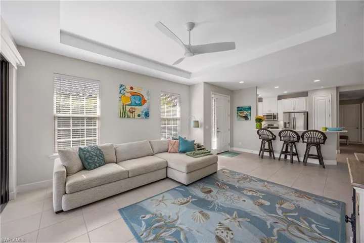 Living room with light tile patterned floors, a raised ceiling, ceiling fan, and recessed lighting