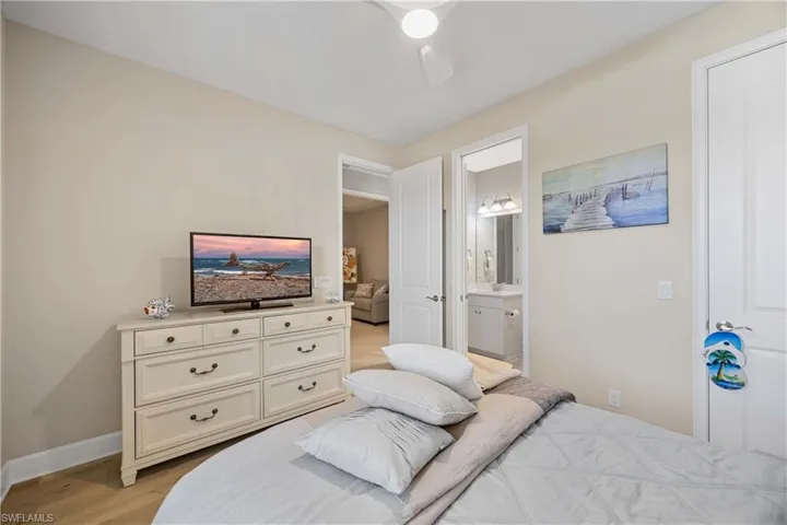 Bedroom with light wood finished floors, ensuite bathroom, and a ceiling fan