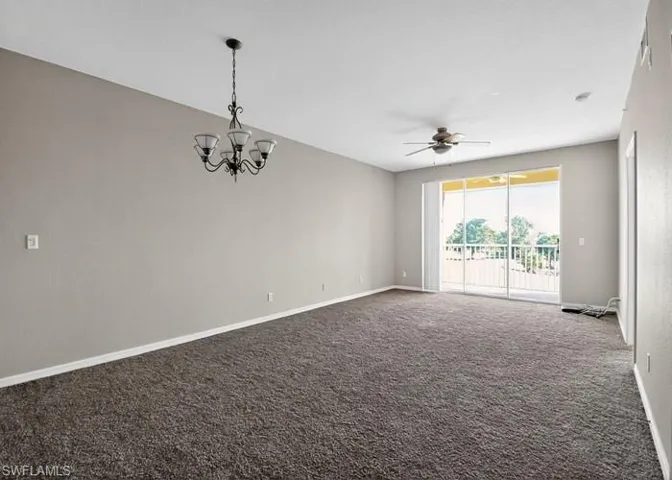 Empty room featuring dark carpet, a chandelier, and a ceiling fan