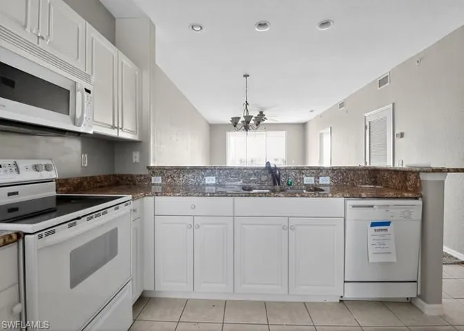 Kitchen featuring white appliances, white cabinetry, a textured wall, dark stone countertops, and light tile patterned floors