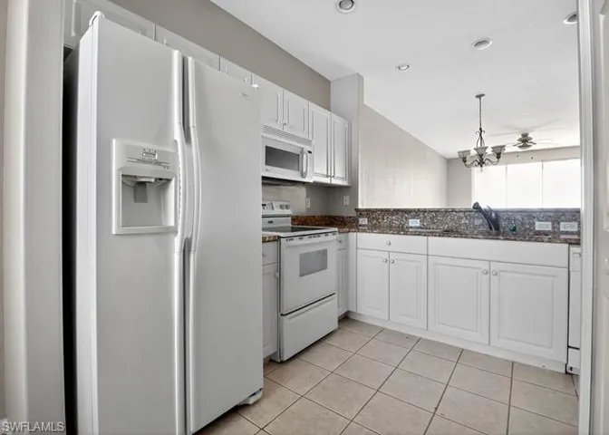 Kitchen with white appliances, white cabinetry, hanging light fixtures, light tile patterned flooring, and dark stone counters