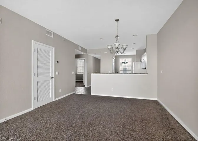 Empty room featuring a chandelier and dark colored carpet