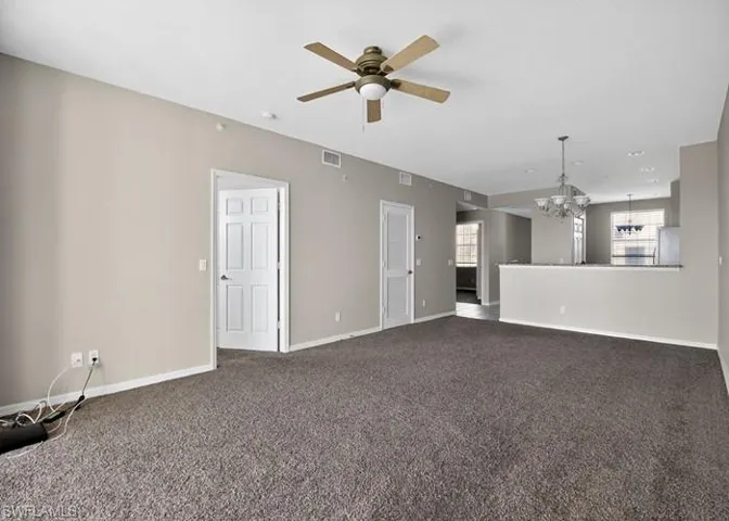 Unfurnished living room featuring a chandelier, a ceiling fan, and dark colored carpet
